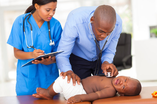 african pediatrician with nurse assistant examining a child