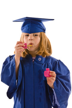 Young graduate in cap and gown blowing bubbles