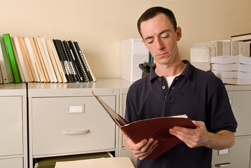 Caucasian male in file room reading papers inside a folder