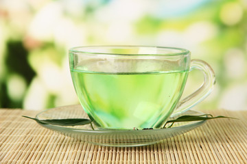 Transparent cup of green tea on bamboo mat, on nature