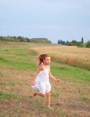 Fototapeta na wymiar Pretty little girl running on the grass on cloudy spring day