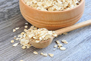 Oat flakes in bowl and wooden spoon on old wooden background