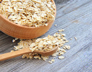 Oat flakes in bowl and wooden spoon on old wooden background
