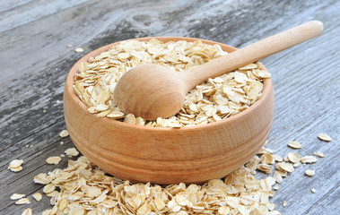 Oat flakes in bowl and wooden spoon on old wooden background