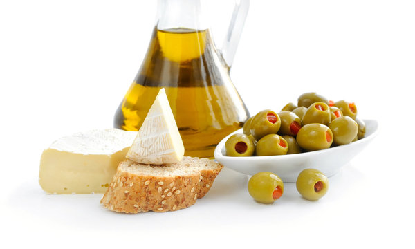 Green olives, oil, slices of bread and cheese are on a white