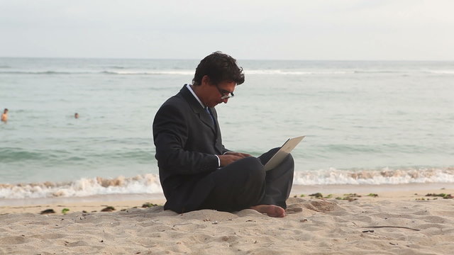 Handsome businessman sitting at beach and typing on laptop