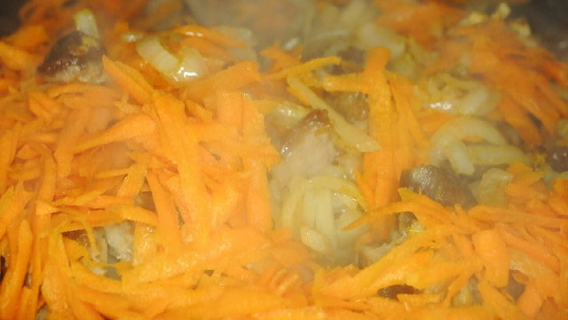 Turning over frying meat on pan with carrot and onion