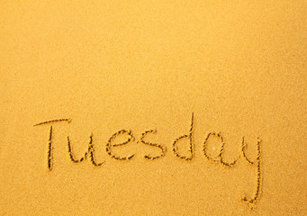 Tuesday, written in sand on beach texture.