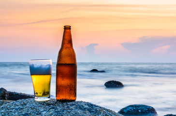 Glass of beer and a bottle on the rock at sea