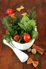 Herbs and spices in ceramic mortar, on wooden background