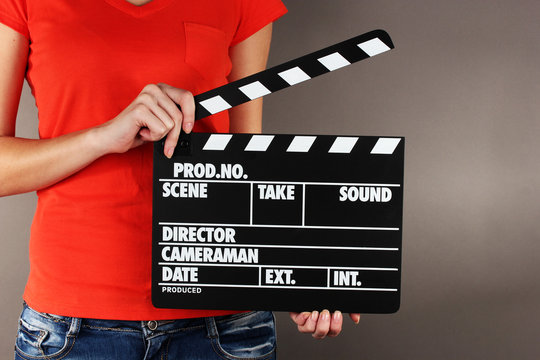 Movie production clapper board in hands on grey background