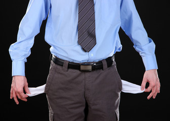 Business man showing his empty pockets, on black background