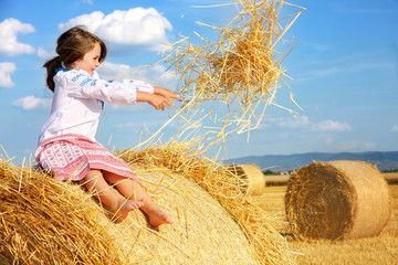 small rural girl on harvest field with straw bales