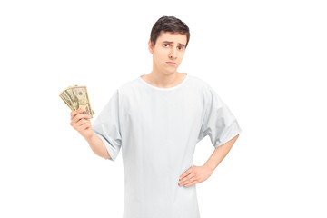 A sad male patient in a hospital gown holding US dollars