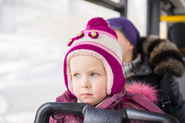 Adorable girl with mother ride on modern city bus in sunny winte