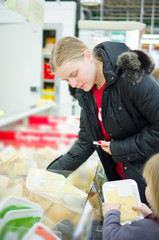 Young mother with daughter select cheese in fridge in supermarke