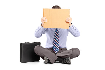 Businessman sitting on ground and hiding his face with a piece o