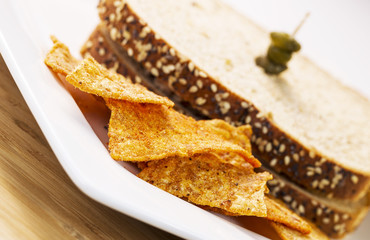 Golden Chips in front of Sandwich on White Plate