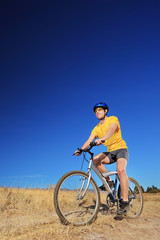 A young male with yellow shirt and helmet riding a mountain bike