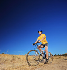 A young male with yellow shirt and helmet riding a mountain bike