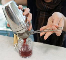 Bartender is straining cocktail into glass