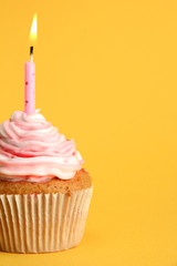 tasty birthday cupcake with candle, on yellow background