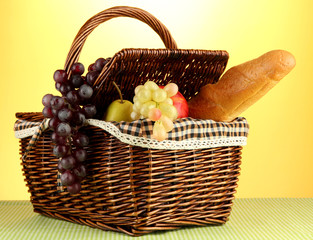 Picnic basket with fruits on cloth on yellow background