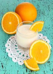 Delicious yogurt in glass with orange on wooden table close-up