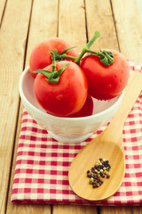 Fresh tomatoes in white bowl over wooden background