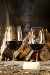 Copas de vino tinto con chimenea y fuego de fondo.