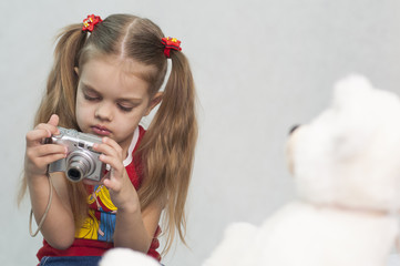 Девочка фотографирует мишку цифровым фотоаппаратом