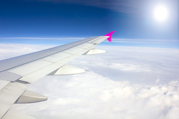Obraz premium Wing of airplane flying above the clouds with sunlight backgrou