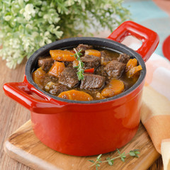 stew of beef with vegetables and prunes in a red cast iron pan