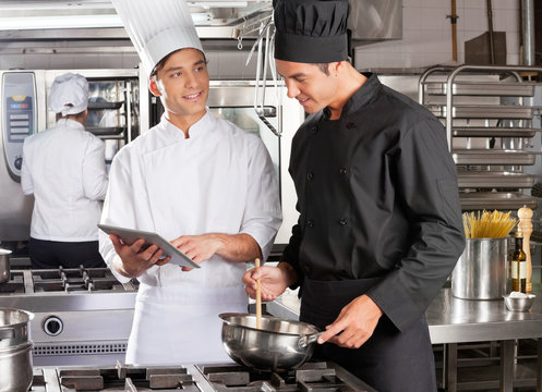 Male Chef Assisting Colleague In Preparing Food - Powered by Adobe