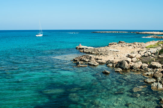 Seashore of Cyprus island with rocky coast and white yacht