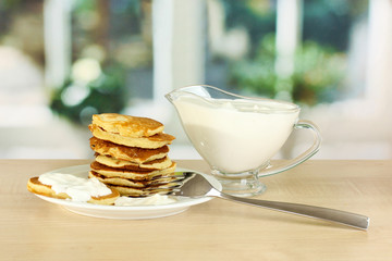 Sweet pancakes on plate with sour cream on table in kitchen
