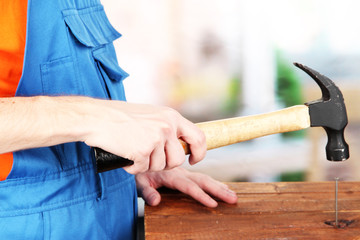Builder hammering nails into board on room background
