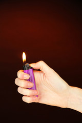 Burning lighter in female hand, on dark brown background