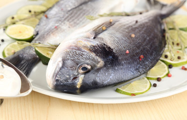 Two fish dorado with lemon on plate on wooden table close-up