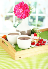 Cups of tea with flower and cake on wooden tray on table in