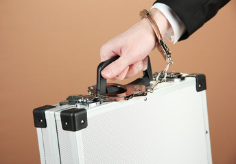 Hand with handcuff and suitcase, on color background
