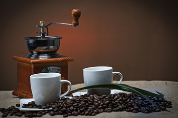 Tazas de café y molinillo clásico sobre granos naturales.