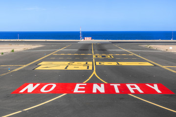no entry sign at the runway of the airport with ocean in backgro