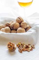Close up of a heap of dry tasty walnuts on a table with tablecloth, and a glass of white wine