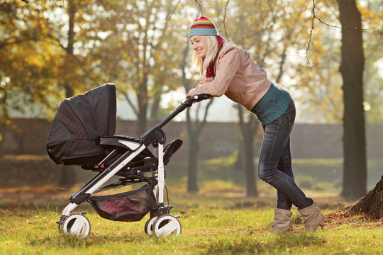 Young mother with a baby carriage walking in a park