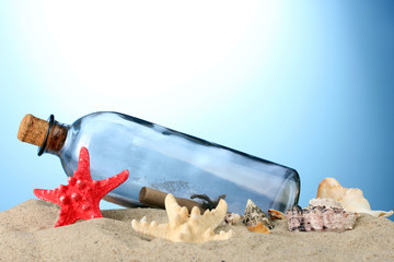 Fototapeta na wymiar Szklana butelka z uwagą wewnątrz na piasku, na niebieskim tle
