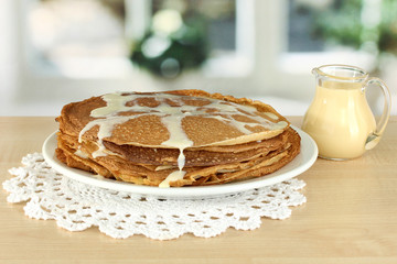 Sweet pancakes on plate with condensed milk on table in kitchen