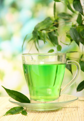 Transparent cup of green tea on bamboo mat, on nature