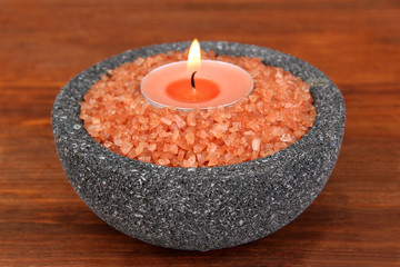 Candle in stone bowl with marine salt, on wooden background