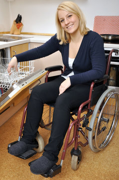 Junge Frau im Rollstuhl räumt Spülmaschine aus